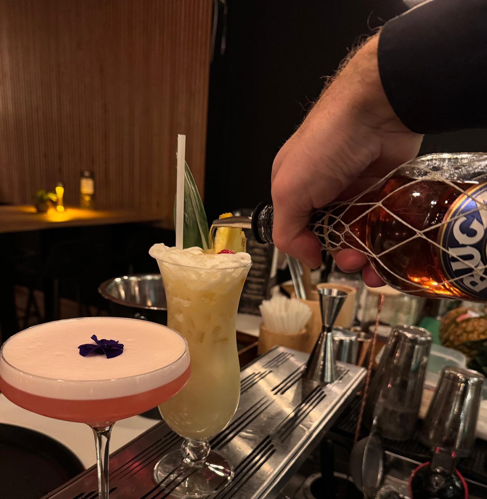 Bartender pouring Brugal rum next to two signature cocktails